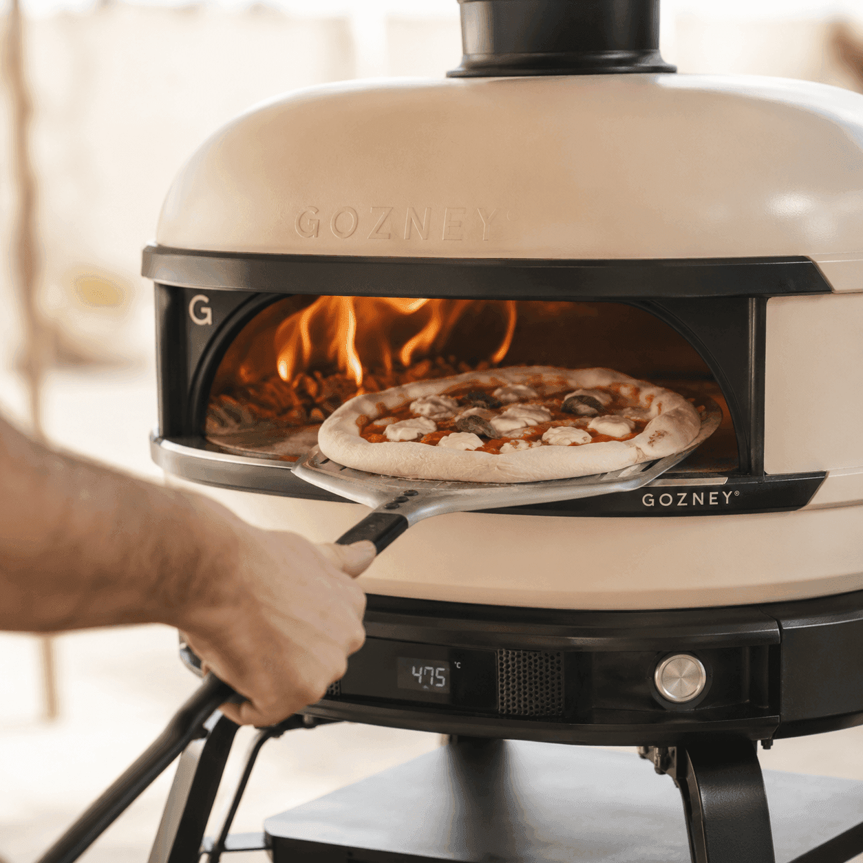 Pizzaiolo schiebt eine Pizza mit der Schaufel in den lodernden Ofen